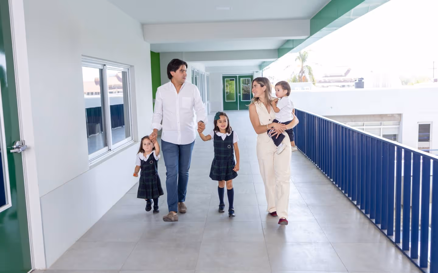 Familia con dos niñas en uniformes escolares y un niño pequeño caminando juntos en un pasillo escolar.