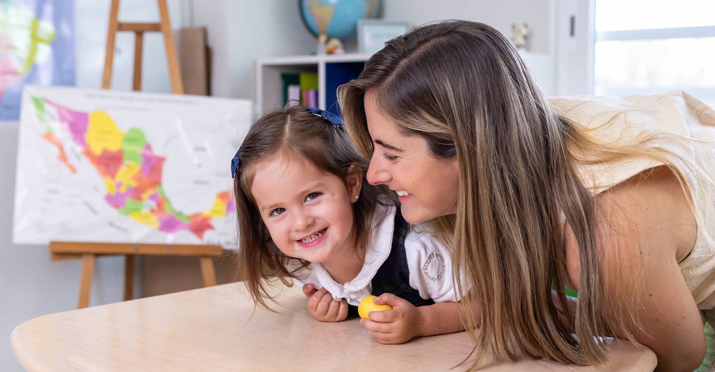 Madre e hija sonriendo en el aula junto a un mapa de México.