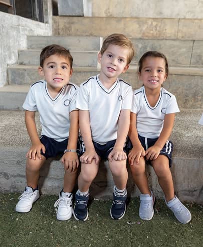 Niños sonrientes sentados en escalones con uniforme escolar deportivo.